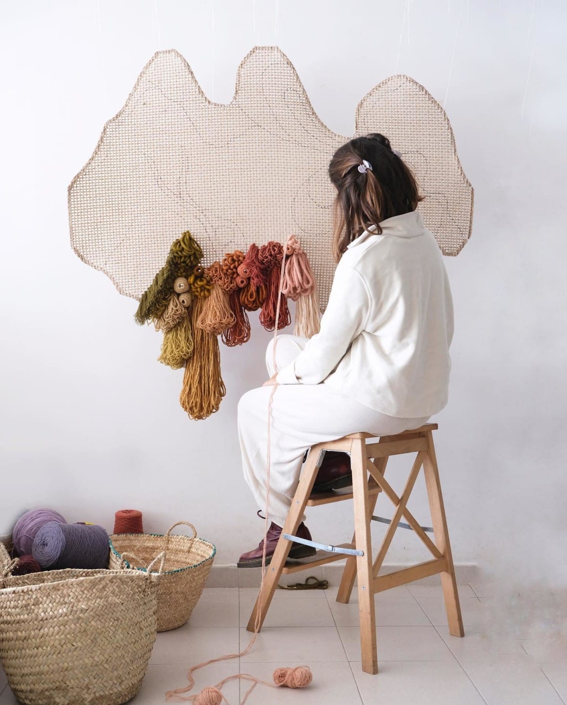 on voit l'artiste en train de réaliser une oeuvre avec des bobines de fil et de laine
