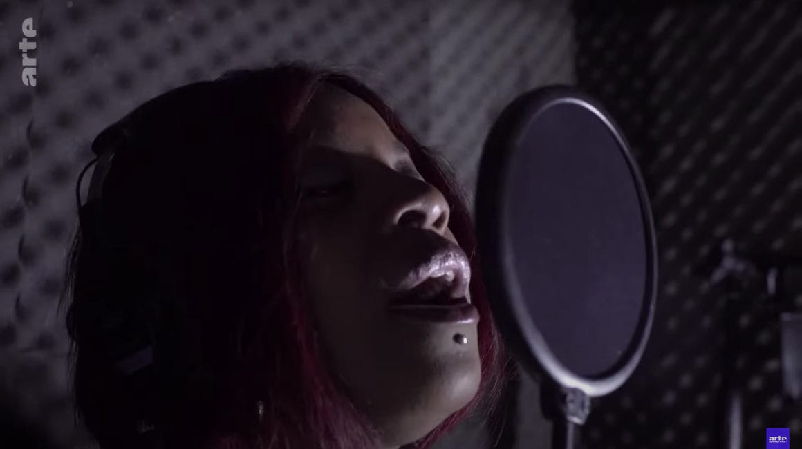 Capture d'écran de l'épisode 3, où l'on voit la chanteuse K Reen chanter en studio dans une cabine de mousse acoustique