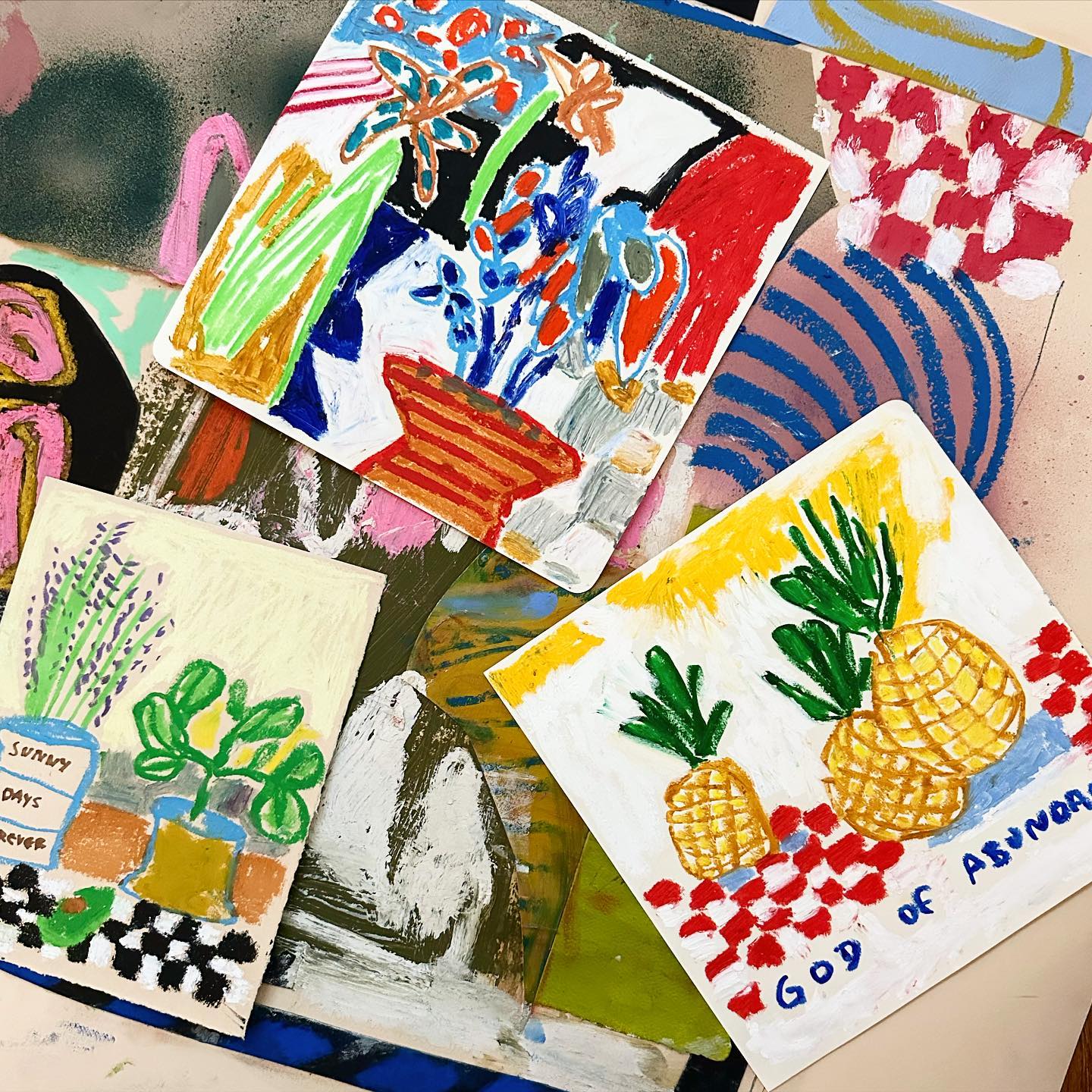 Plusieurs dessins très colorés sur un plan de travail. On observe des éléments tels que des vases avec des fleurs, des ananas etc.