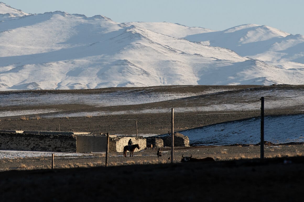 A horse and rider stand outside a small home against the backdrop of the snow-covered Altai Mountains of western Mongolia © Claire Thomas