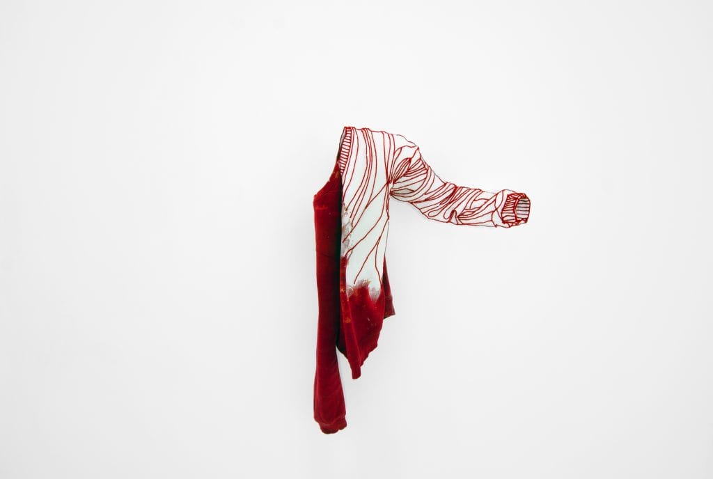 Vêtement rouge suspendu, silhouette absente. © Bastien Cuénot
