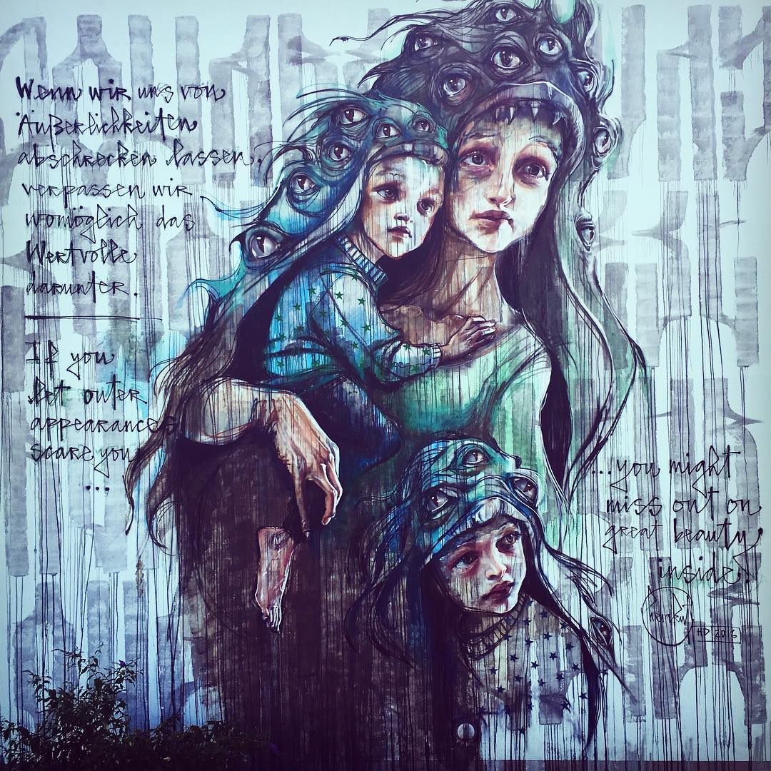Fresque réaliser par le duo Herakut. Une mère et ses deux enfants portent des peaux de monstres par dessus leurs vêtements. La mère porte dans ses bras l'un de ses enfants et l'autre est accroché contre elle au niveau de la taille.