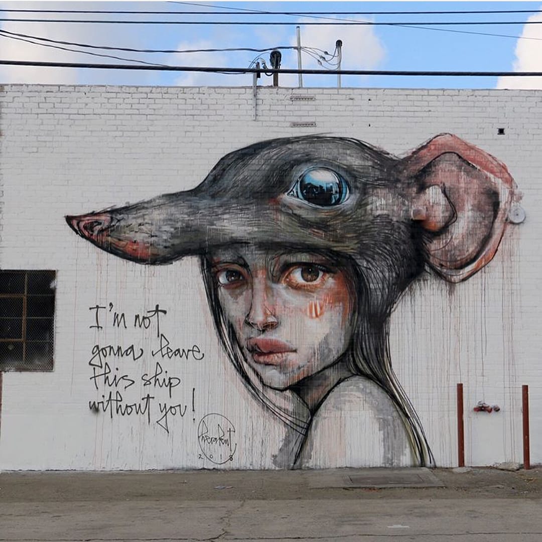 Fresque réaliser par le duo Herakut. une petite fille a sur sa tête une tête de rat comme un chapeau, la petite fille nous regarde l'air triste.