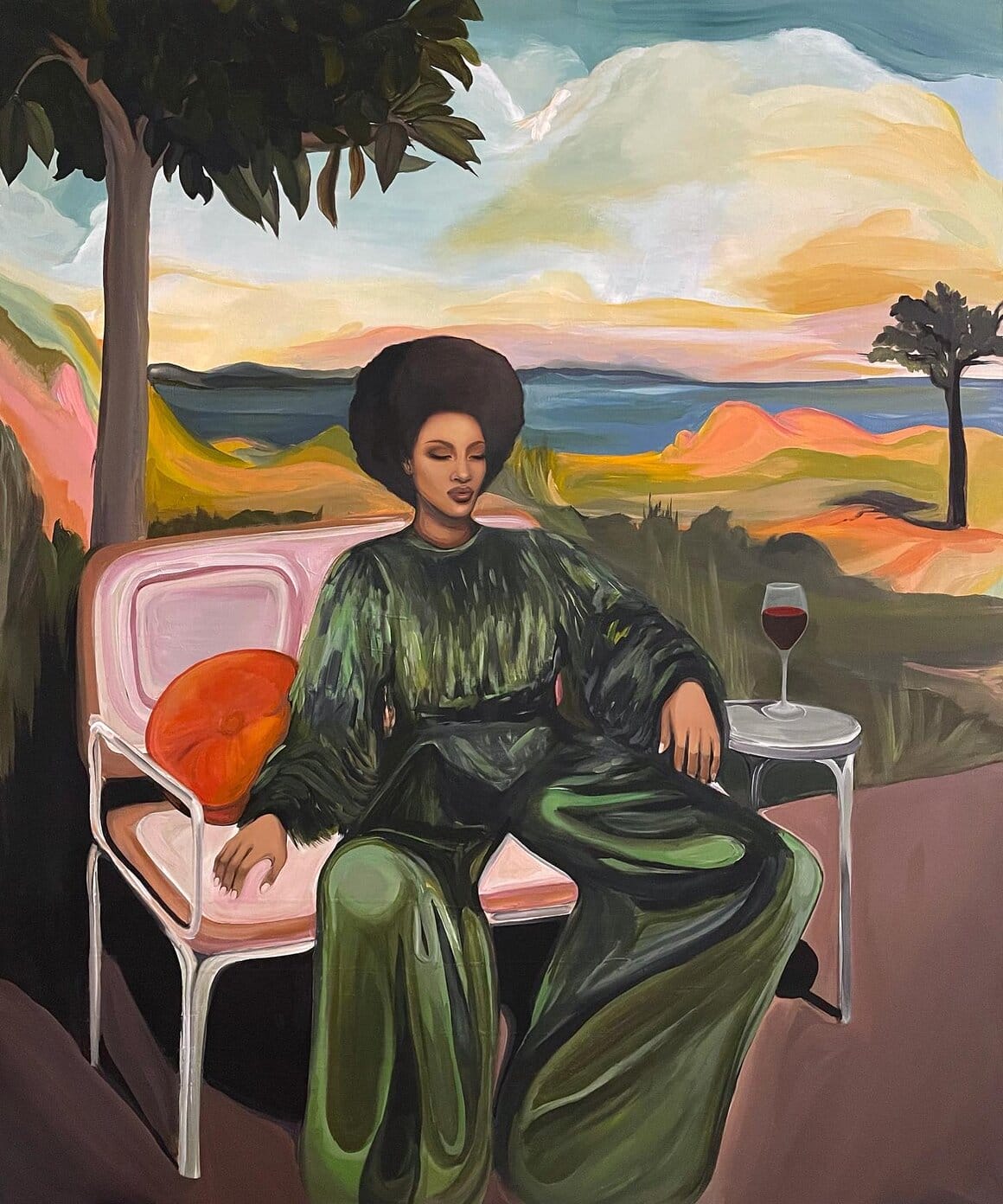 Femme noire vêtue d’un ensemble vert ample, assise dans un fauteuil avec un verre de vin posé à côté d’elle, face à un paysage coloré.