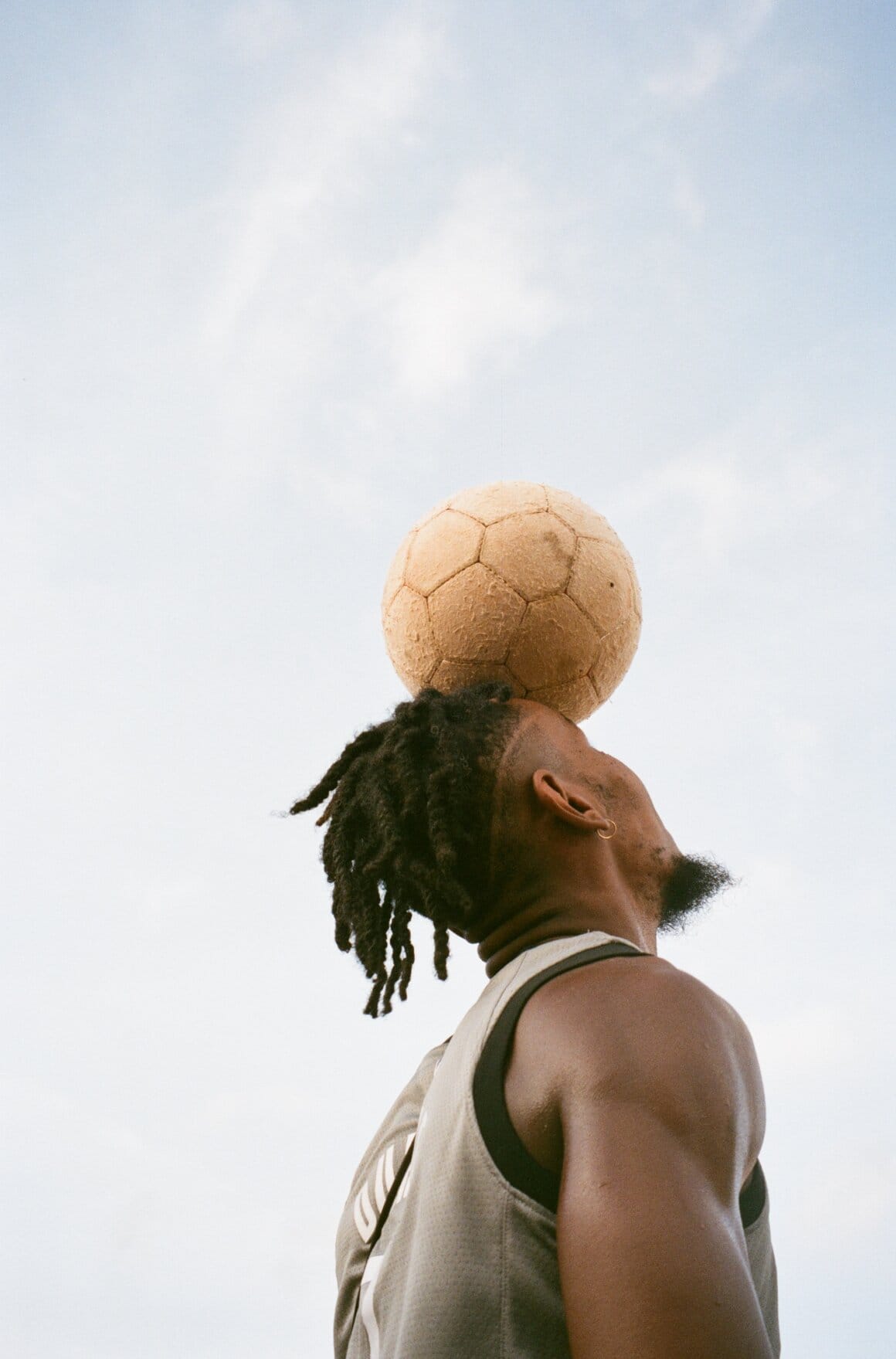 Un homme de profil maintient un ballon de football en équilibre sur son front.
