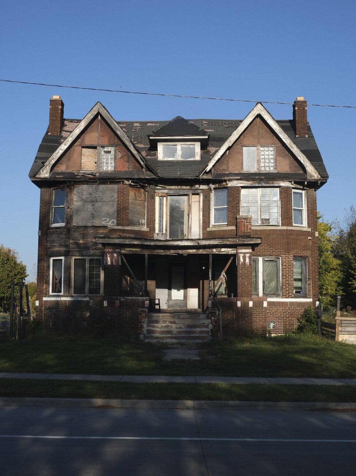 Une grande maison partiellement condamnée et dégradée se dresse au bord d’une route.