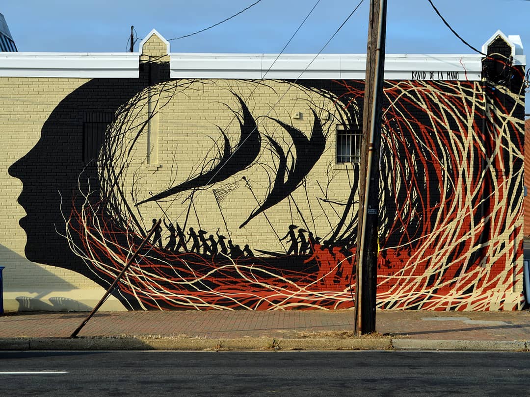 Fresque réaliser par la street artiste David de la mano. "change begin inside" représente la silouhette d'un visage avec derrière son visage des personnes brandissant ce qui semble être des armes ou des outils d'agriculture comme un râteau