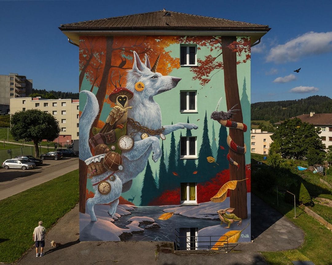 Œuvre réalisé par l'artiste Dulk. la fresque représente un loup ou un chien blanc debout sur ses deux pattes portant plein d'horloges sur lui, il possède une corne sur la tête. Sur son dos une chouette avec un chapeau de champignon sur la tête, en face d'eux sur un arbre un serpent avec une tête de tricératops et au pied de l'arbre un lapin grenouille.