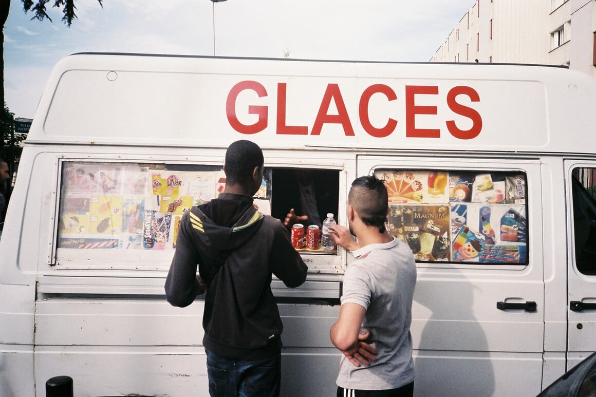 Deux hommes se tiennent devant un camion de glaces blanc garé dans une rue.